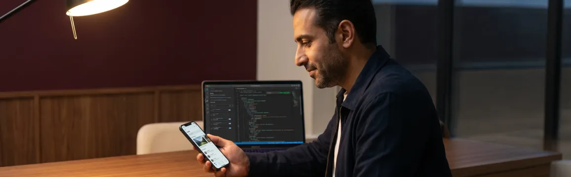 Mobile developer reviewing cross-platform app output on phone at desk during evening hours with warm focused light Mobile developer reviewing cross-platform app output on phone at desk during evening hours with warm focused light