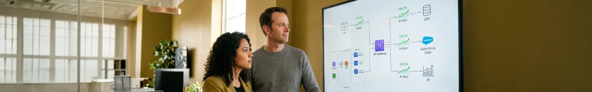 Integration team reviewing unified API dashboard showing ERP, Salesforce, and BI data in sync on large monitors in modern office with natural light Integration team reviewing unified API dashboard showing ERP, Salesforce, and BI data in sync on large monitors in modern office with natural light