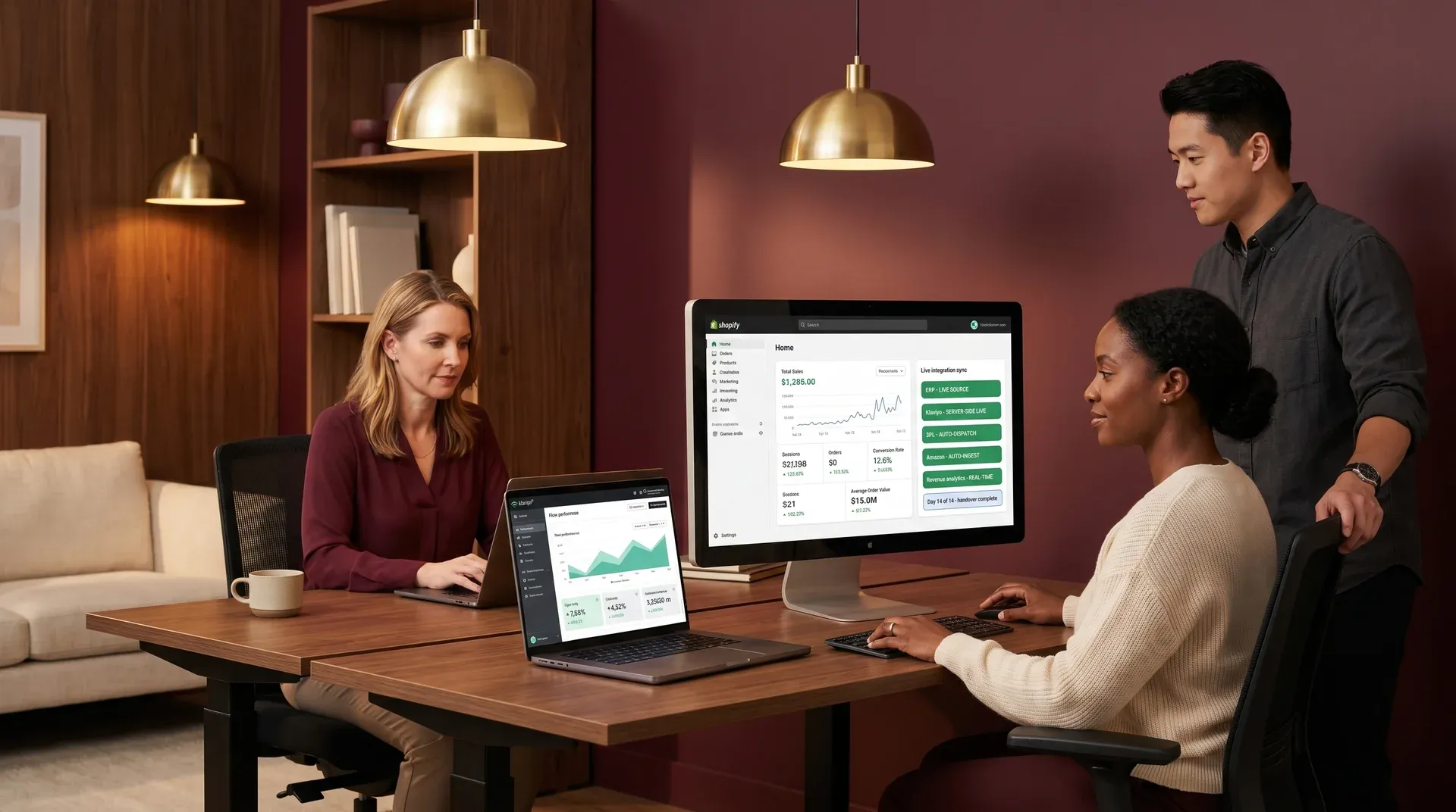Shopify merchant team at integration go-live handover moment with multiple screens showing live Shopify admin and Klaviyo flow analytics dashboards, deep burgundy and walnut ambient office light