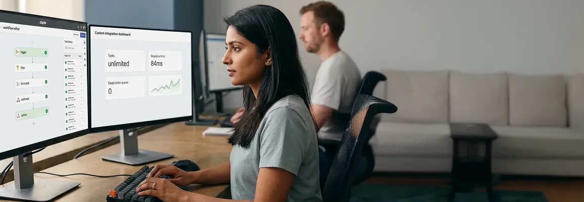 Integration analyst at dual monitors reviewing Zapier workflow map and custom integration dashboard side by side, warm natural office light Integration analyst at dual monitors reviewing Zapier workflow map and custom integration dashboard side by side, warm natural office light